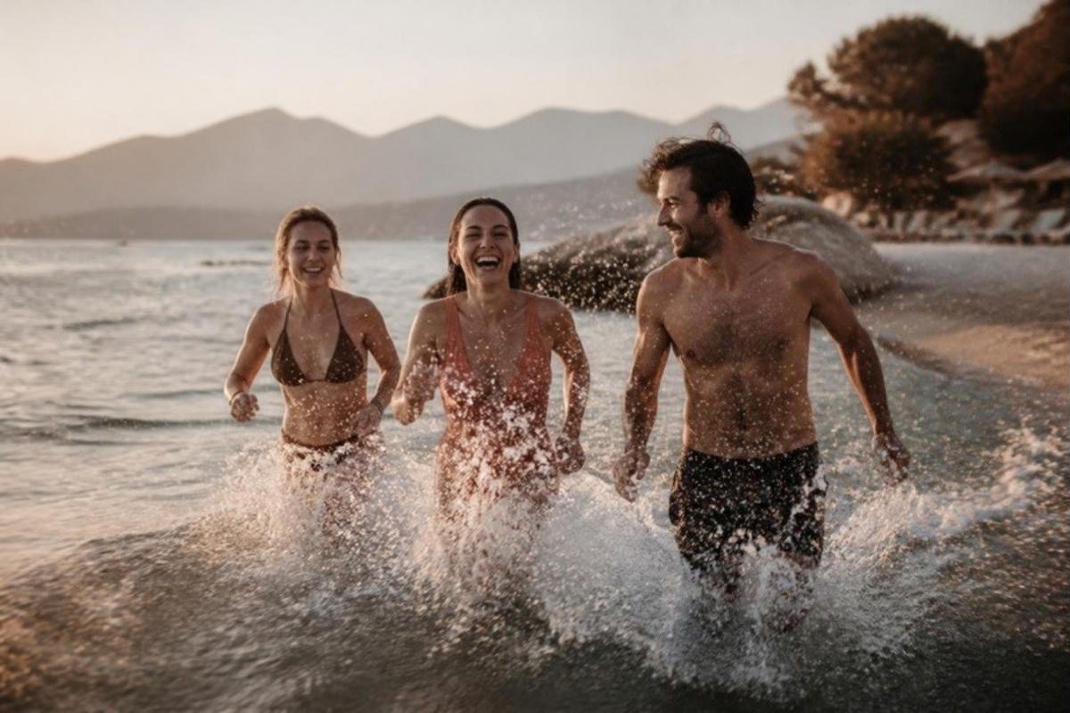 Φίλοι τρέχουν γελώντας μέσα στη θάλασσα, πιτσιλίζοντας νερό, ένα καλοκαιρινό απόγευμα.